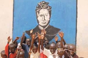 Children raise their hands in front of a mural of St. Bakhita at  a displacement camp  near Khartoum